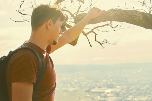 Traveler young man with backpack looking at the city from hill. Concept of tranquil life from the urban bustle. Image with sunlight effect
