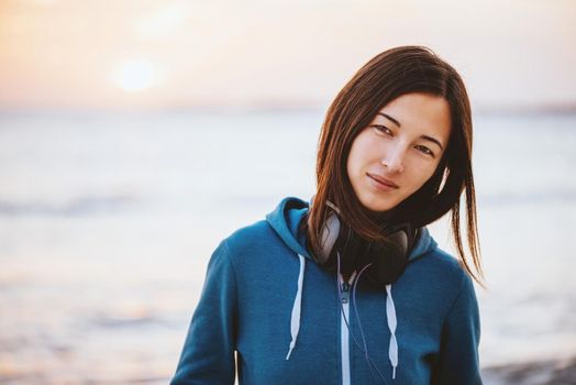 Portrait of beautiful young woman with headphones on background of sea at sunset