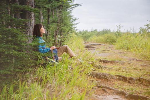 Hiker young woman with backpack resting near the tree in summer forest