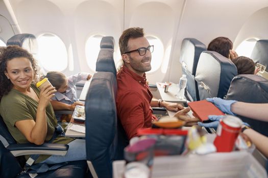 Happy passengers smiling while female flight attendant serving lunch on board. Travel, service, transportation, airplane concept