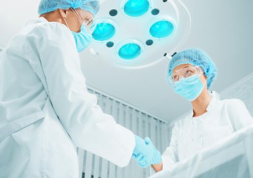 Man surgeon shakes hand with woman surgeon in operating room. Focus on man surgeon.