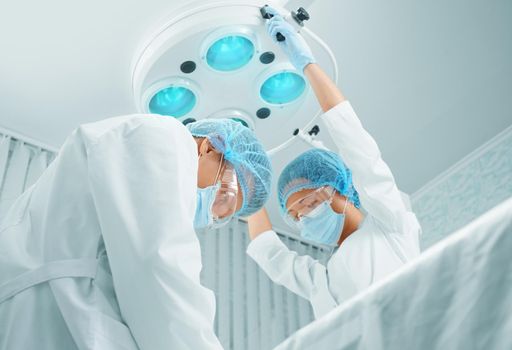 Man surgeon and female assistant working in operating room. Focus on man surgeon.