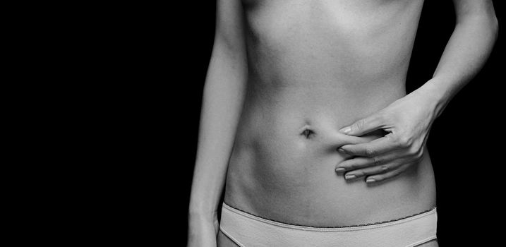 Unrecognizable woman holds a fold of skin on belly, monochrome image