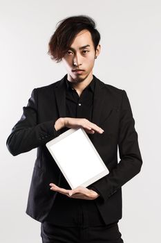 Serious young male executive using digital tablet against gray background