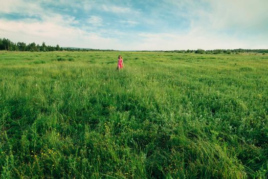 Happy little girl in pink dress walking on summer green meadow