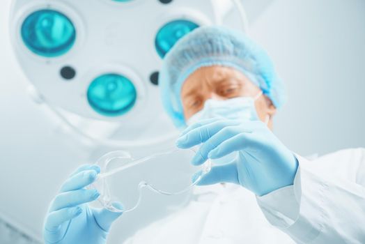 Young male surgeon doctor takes off his protective glasses in operating room, focus on glasses