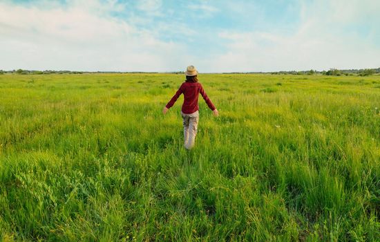 Unrecognizable hipster girl in straw hat walking on summer meadow, rear view. Concept of happiness and carefree