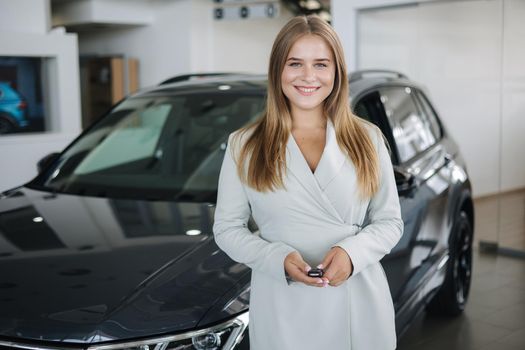 Portrait of beautiful and young business woman in car showroom. Female hold keys from mher new car.