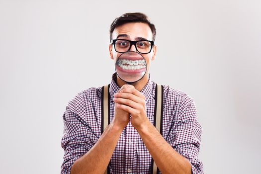 Portrait of nerdy man is showing his braces with magnifying glass.