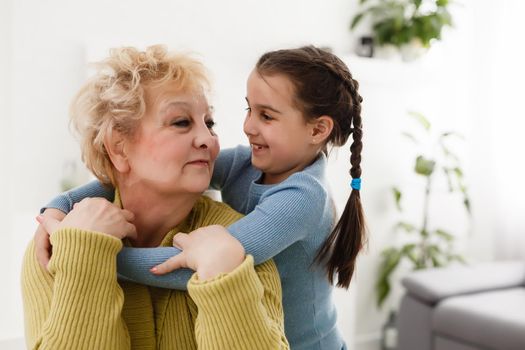 Senior woman hugging granddaughter while sitting on sofa at home