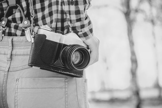 Old photo camera is hanging on female shoulder. With film grain and low contrast effect. Black-white photo.