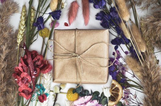 Gift box wrapped in eco friendly craft paper surrounded with colorful fresh dried flowers top view, Spring,Mothers Day,Birthday,greeting card isolated on white background, Flat lay modern design beautiful