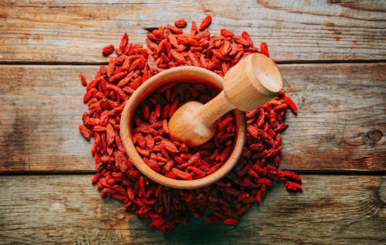 Goji berries in mortar with pestle on wooden background, top view