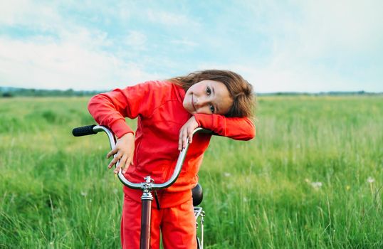 Cute smiling little girl standing with a bicycle on green meadow in summer, healthy lifestyle