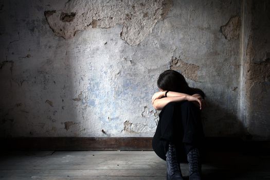 Depressed and lonely girl sitting alone in a spooky abandoned dirty old room on the wooden floor feeling miserable and anxiety cry over her life, depression and addiction issues concept with copy space shadows and dark place