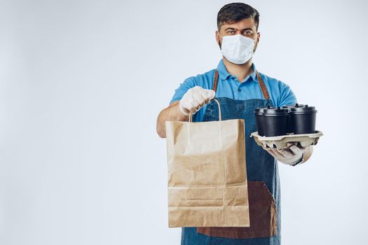 Delivery man in protective mask and medical gloves holding takeaway food. Compliance with the hygiene rules while covid-19 pandemic. Safe service