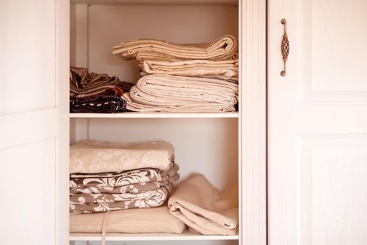 A beautiful white wooden cabinet with door knobs in a vintage retro style, inside are neatly folded towels and bed linens in beige shades.