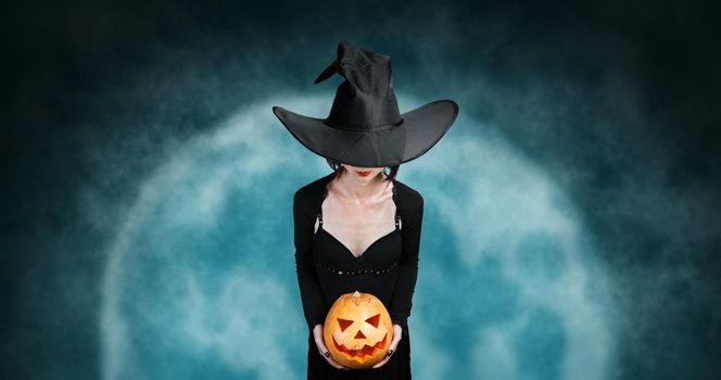 Witch holds Halloween carved pumpkin on background of full moon. Halloween, horror theme