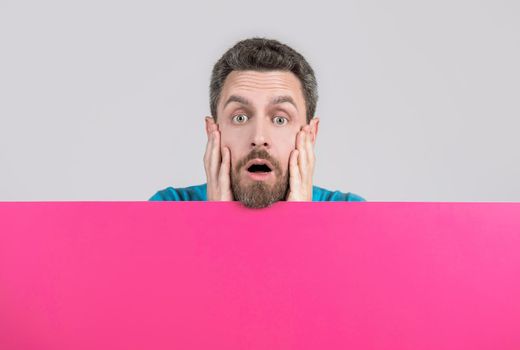 surprised mature bearded man behind blank pink paper banner with copy space for news, discount.