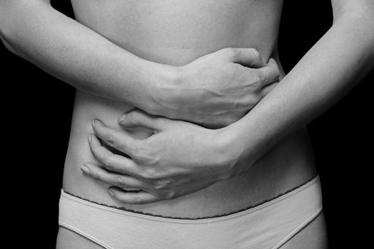 Unrecognizable woman holds her abdomen, abdominal or menstrual pain, monochrome image