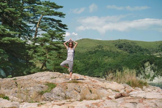 Traveler young woman standing in yoga pose of tree on stone in summer on background of mountains