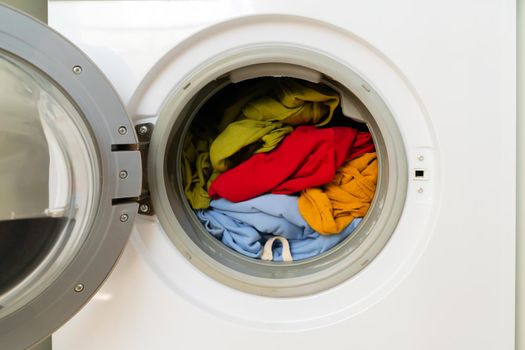 Washing machine with open door and bright colored clothes inside, close-up. view