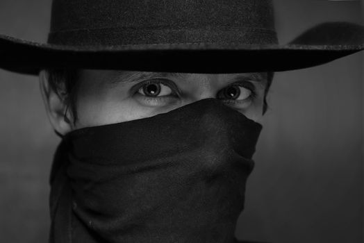 Black-white portrait of a man cowboy with a scarf on his face and in a hat