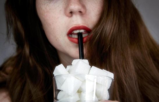 Portrait of young woman drinking with a black colored straw from a glass filled with sugar cubes Junk food, unhealthy diet, too much sugar on drinks, nutrition concept closeup