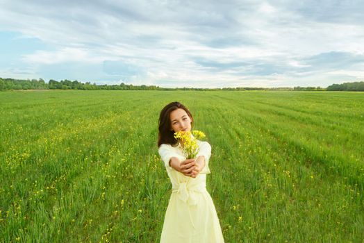 Beautiful young woman holding bouquet of yellow flowers on summer meadow