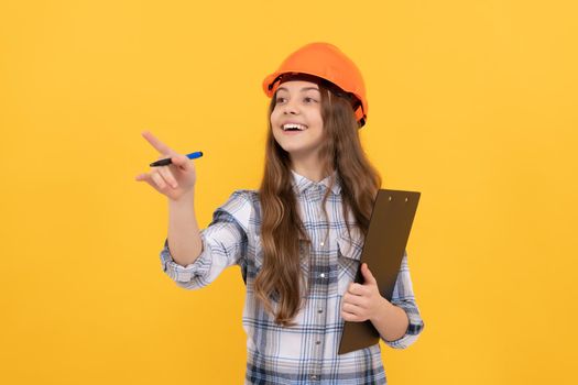 happy labour day. future career. teen girl in helmet making notes. builder kid write in folder. building and construction. happy child worker wear hardhat hold clipboard. pointing finger. childhood.