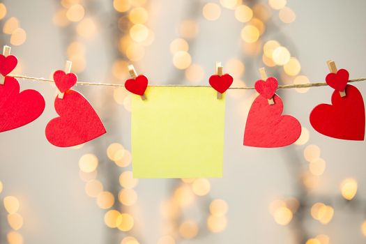 Blank Yellow sticky note hanging with red hearts with bokeh background, romantic Valentines day concept background copy space love