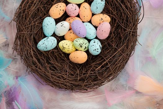 Colorful pastel colored easter eggs in bird's nest top view with bright feasthers top view, April, Easter Holliday, Religion and spring concept background close up