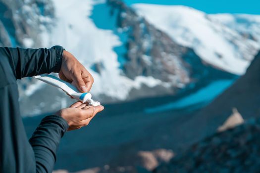 A young man applies sunscreen to his body in the highlands, in the background the peaks of the mountains are covered with snow. The traveler squeezes the cream out of the tube, takes care of his skin.