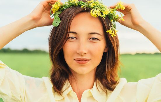 Portrait of attractive brunette young woman with wreath of flowers in summer