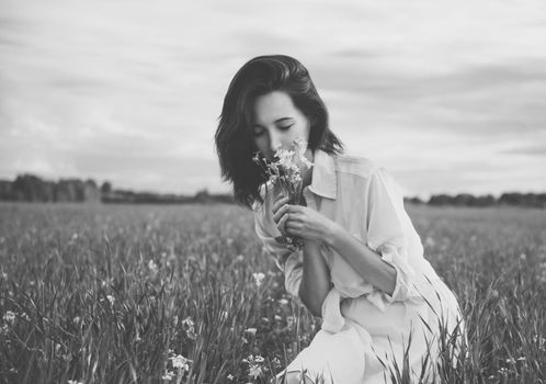 Young beautiful woman picking flowers in a summer meadow. With film grain and low contrast effect. Black-white photo.