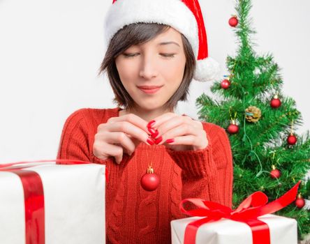 Young woman in santa hat is holding a Christmas red ball on a background of Christmas tree