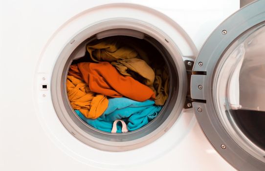 Washing machine with open door and bright colored clothes inside, close-up. view