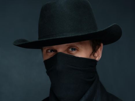 Portrait of a man cowboy with a scarf on his face and in a black hat