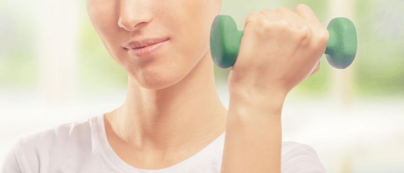 Happy woman is lifting green dumbbell in a gym