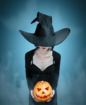 Mystery witch holds Halloween pumpkin on dark background. Halloween, horror theme