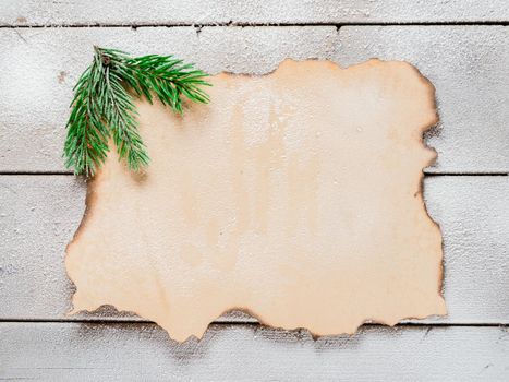 Christmas tree branch on the corner of old paper on a snowy table, copyspace