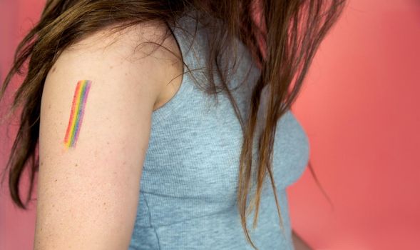 Portrait of a young woman with rainbow Flag on cheek and body, the LGBT community on a colorful pink background freedom, LGBTQ concept beauty