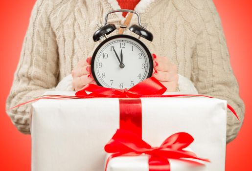 Woman holds clock on the gift box on red background