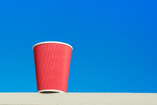 Red paper cup. Blue sky background, copy space