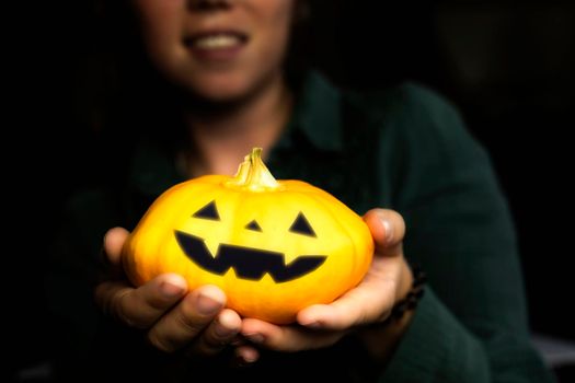 Young girl holding Halloween pumpkin in hands, Jack o Lantern Face with dark shadows, Halloween, Autumn concept spooky