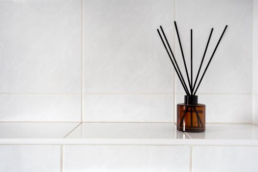 Aromatherapy sticks in glass bottle in toilet or bathroom near white tiled wall with copy space, perfume and bamboo luxury product space for text