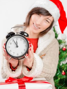 Happy woman shows the clock on the background of the Christmas tree