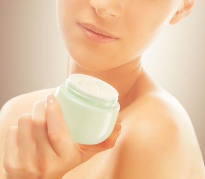 Unrecognizable woman holds a jar of cream near the face