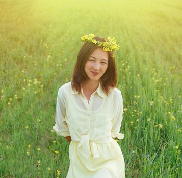 Smiling beautiful brunette young woman with wreath of flowers in summer outdoor