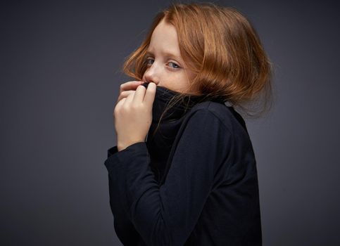 red-haired girl with freckles on her face in a black sweater posing. High quality photo